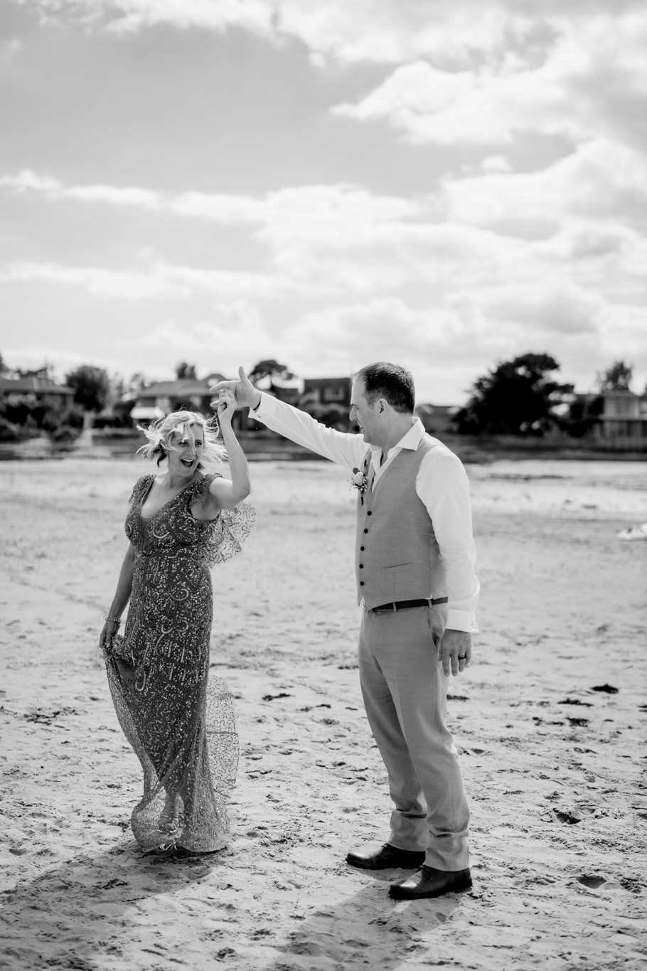 A monochrome image of the groom twirling the bride in a dance motion on the sea