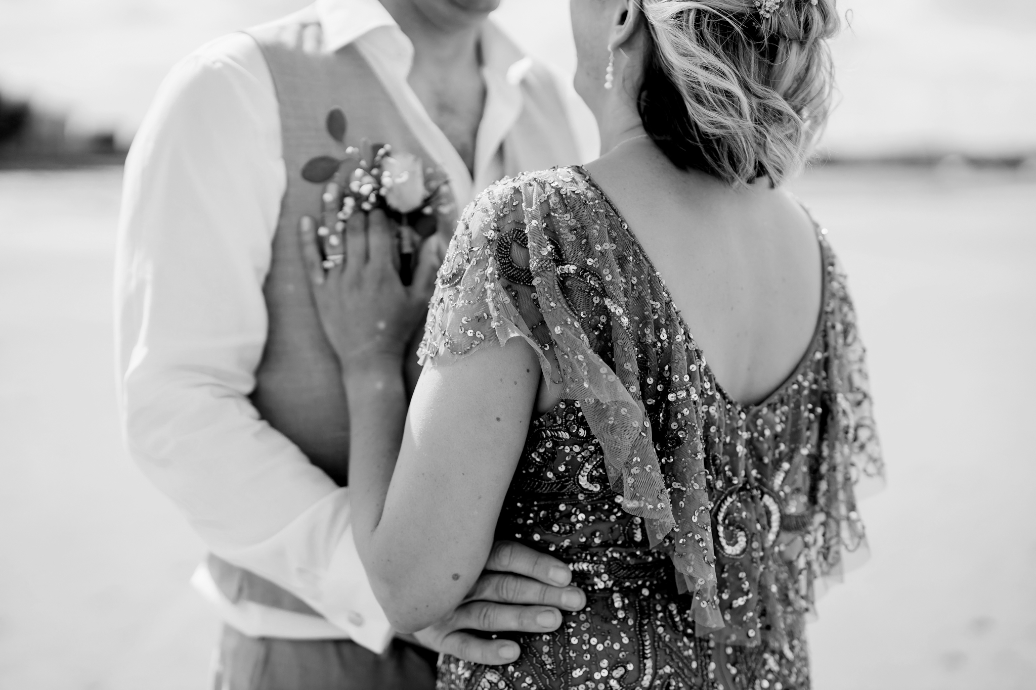A couple standing on a beach wearing a sparkly dress and a suit in monochrome