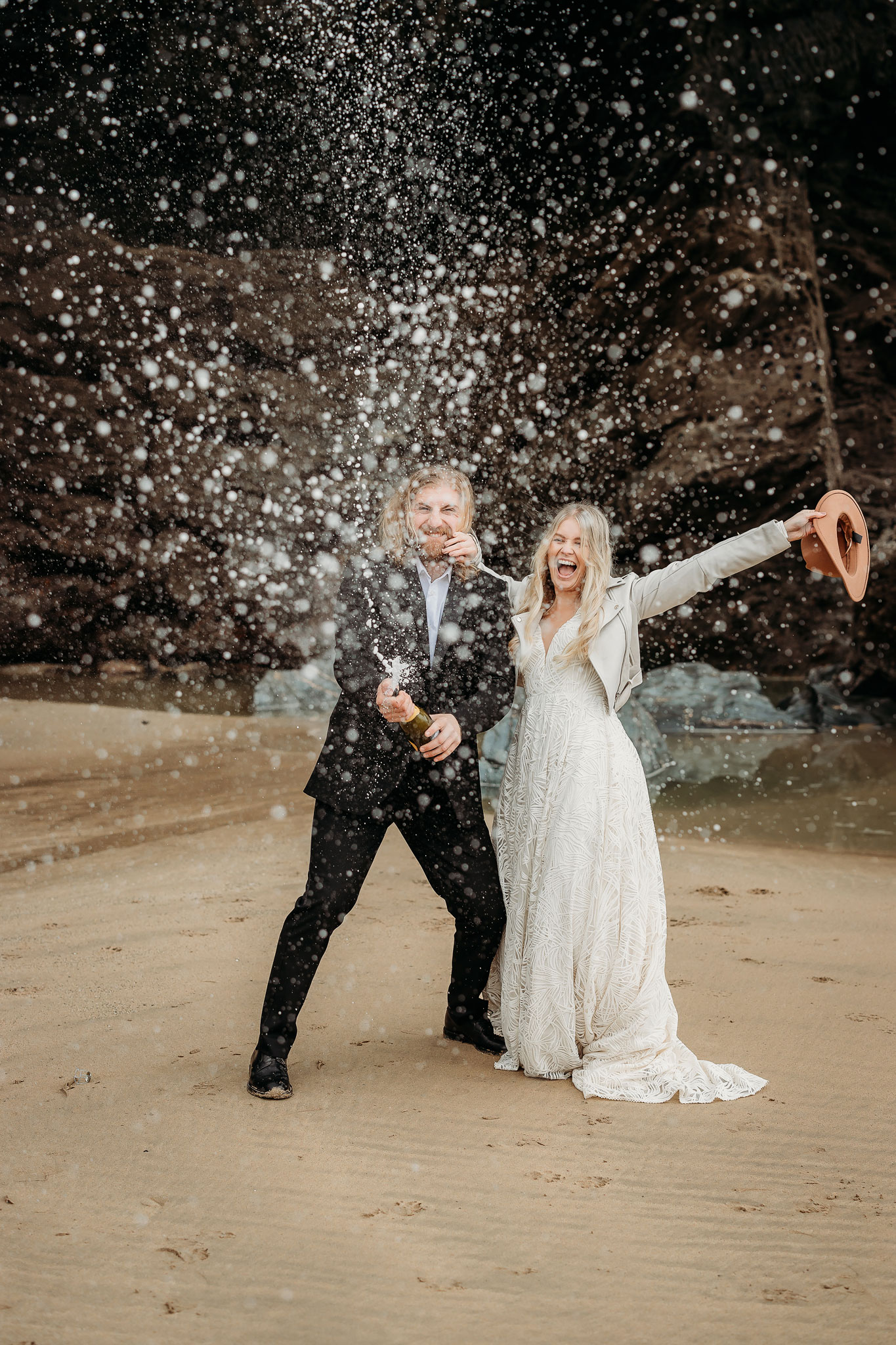 a bride and groom at the beach doing a champagne spray