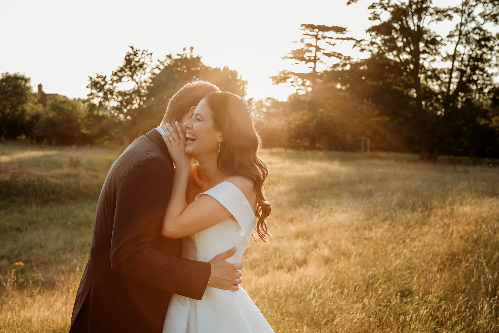 a bride laughing with her husband on a open field at golden hour