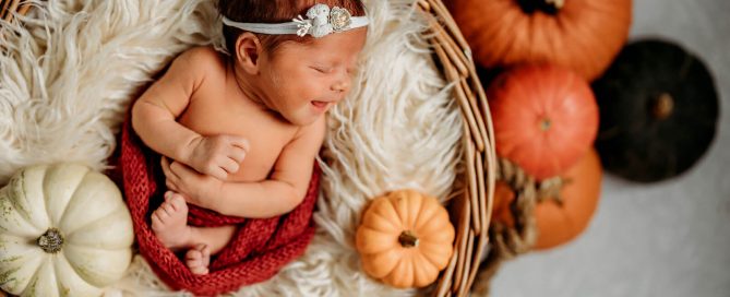 newborn smiling in a basket with pumpkins surrounding her